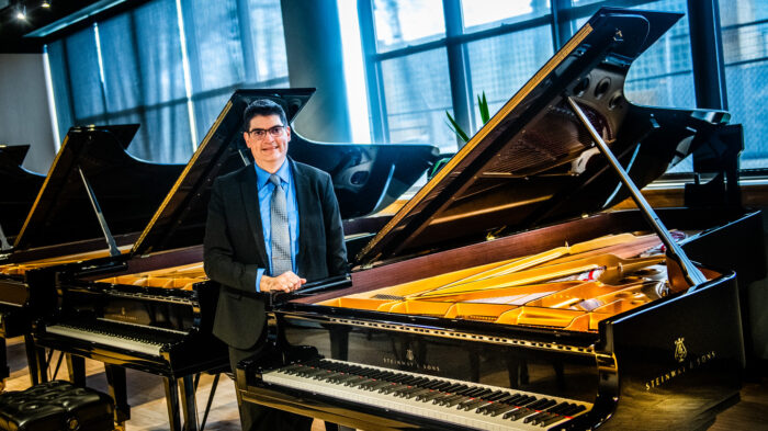 A person in a suit and tie standing near a piano inside of a piano showroom.