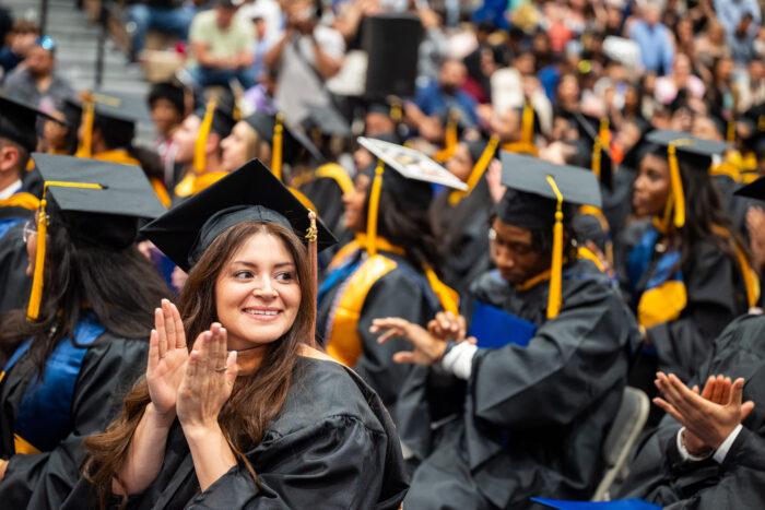 A college graduate in full regalia clapping during a graduation ceremony.