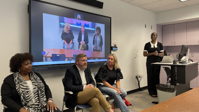 3 people seated during a panel discussion with a moderator.