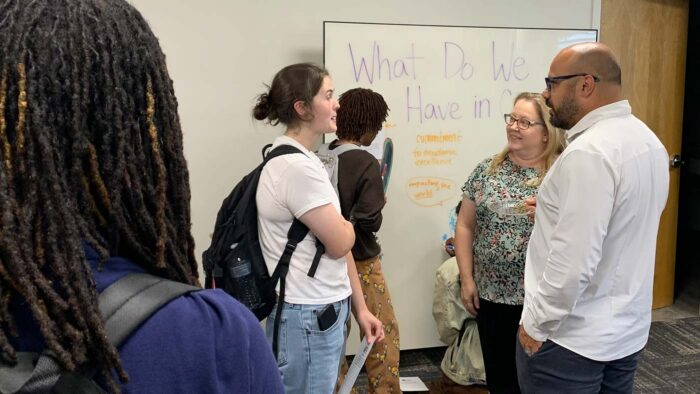 Group of people standing around talking to each other indoors.