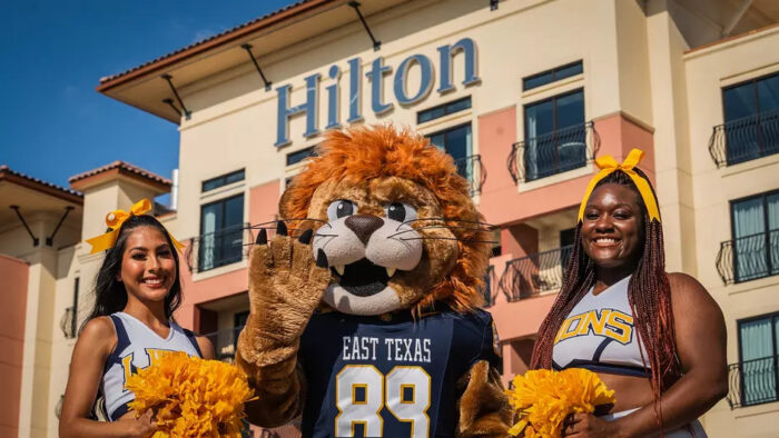 Two cheerleaders and a person in a lion mascot costume pose for a photo.
