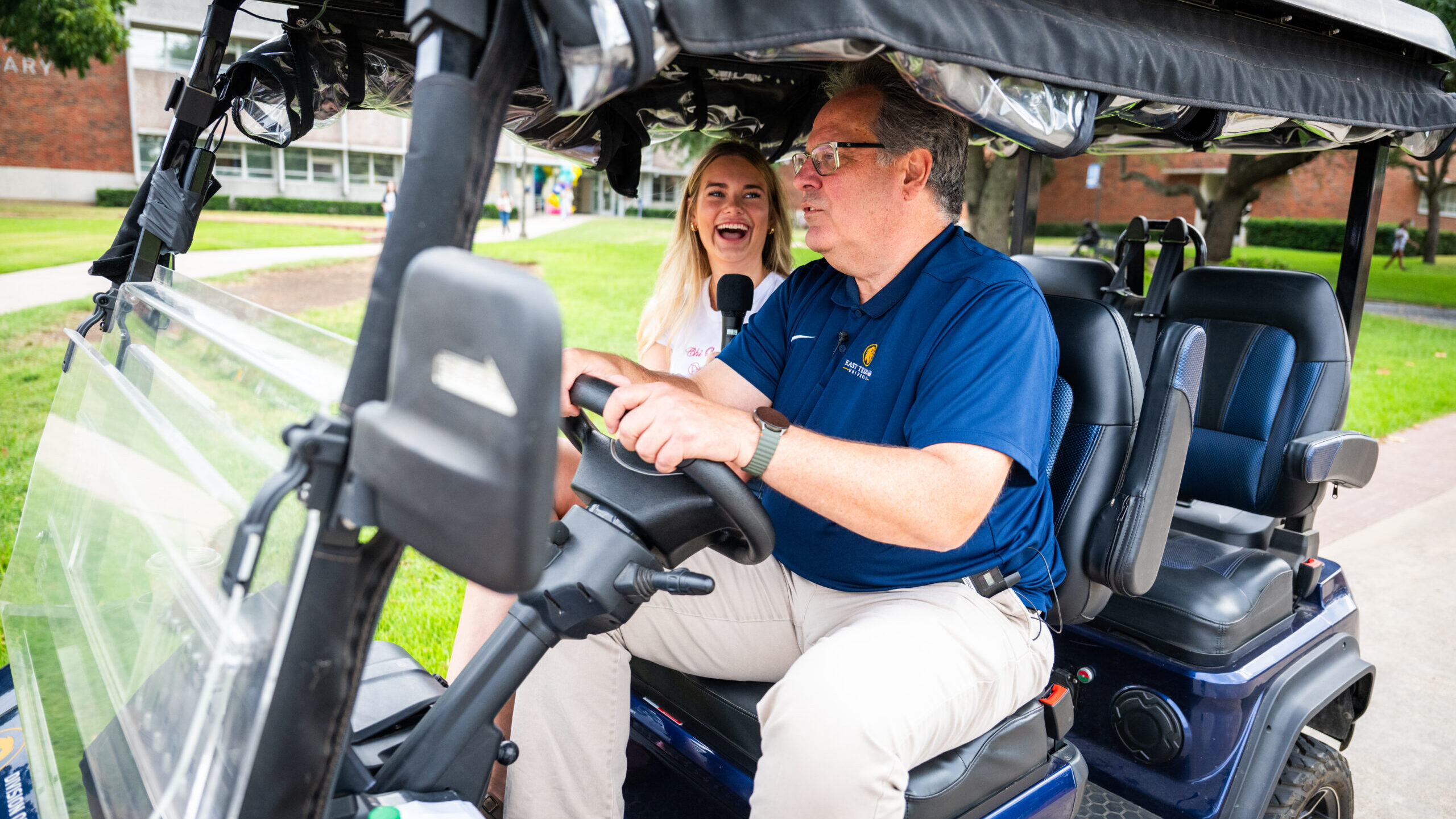 Two people riding in a side-by-side golf cart.