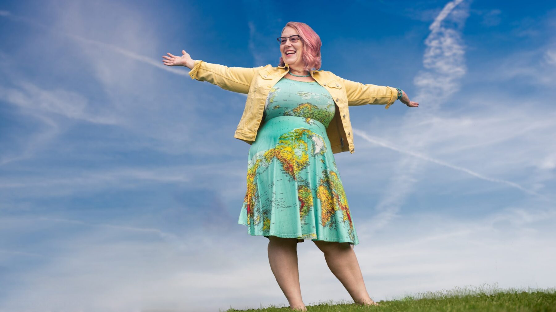 A person in a dress designed with a map motif stands in an open field.