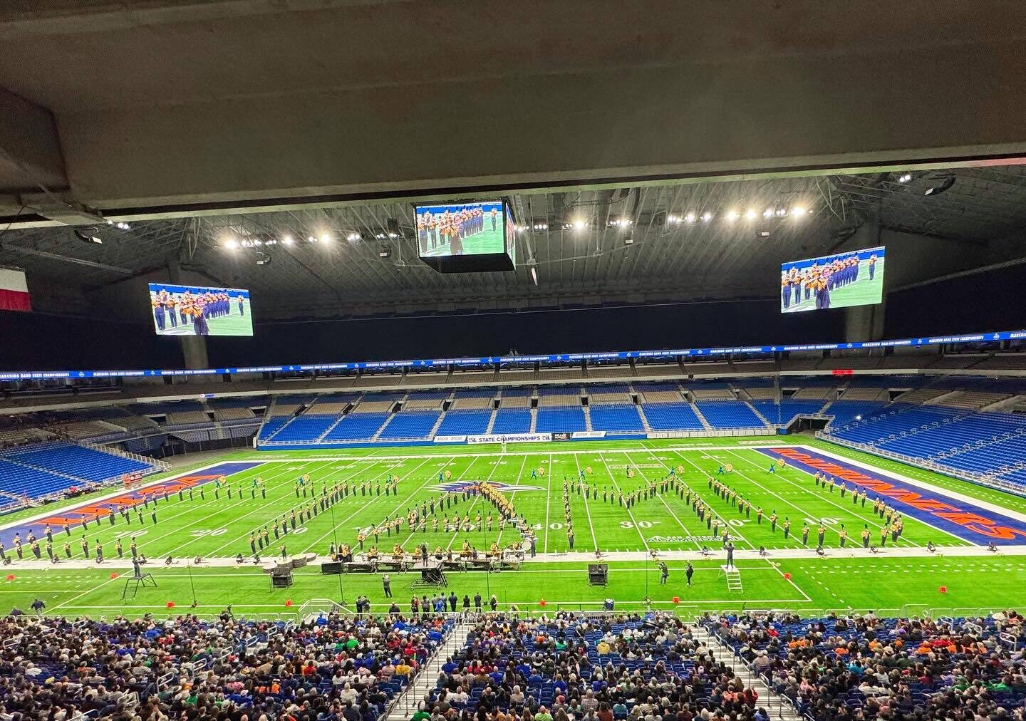 A marching band forms into the shape of the letters ETAMU during a performance in an indoor stadium.