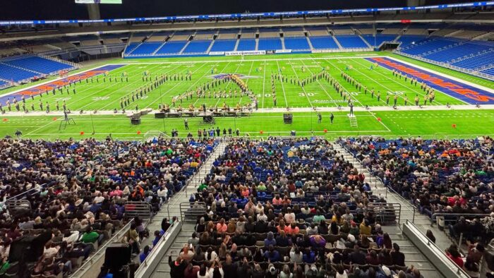 A marching band forms into the shape of the letters ETAMU during a performance in an indoor stadium.