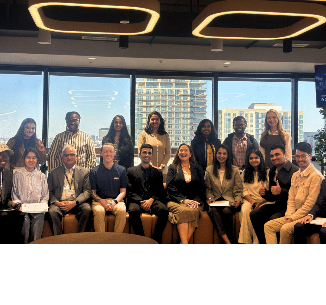 A group of students posing for a photo in front of a large window in a high rise building.