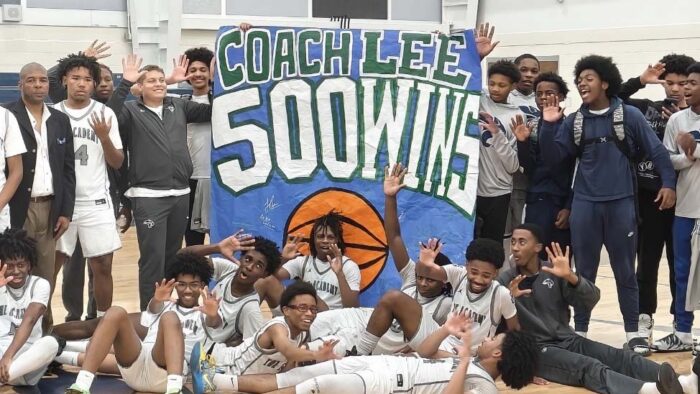 A large group of basket players is gathered around a sign reading "Coach Lee, 500 Wins".