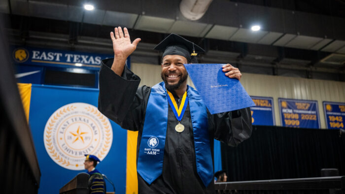 A college graduate smiling with their degree during a graduation ceremony.
