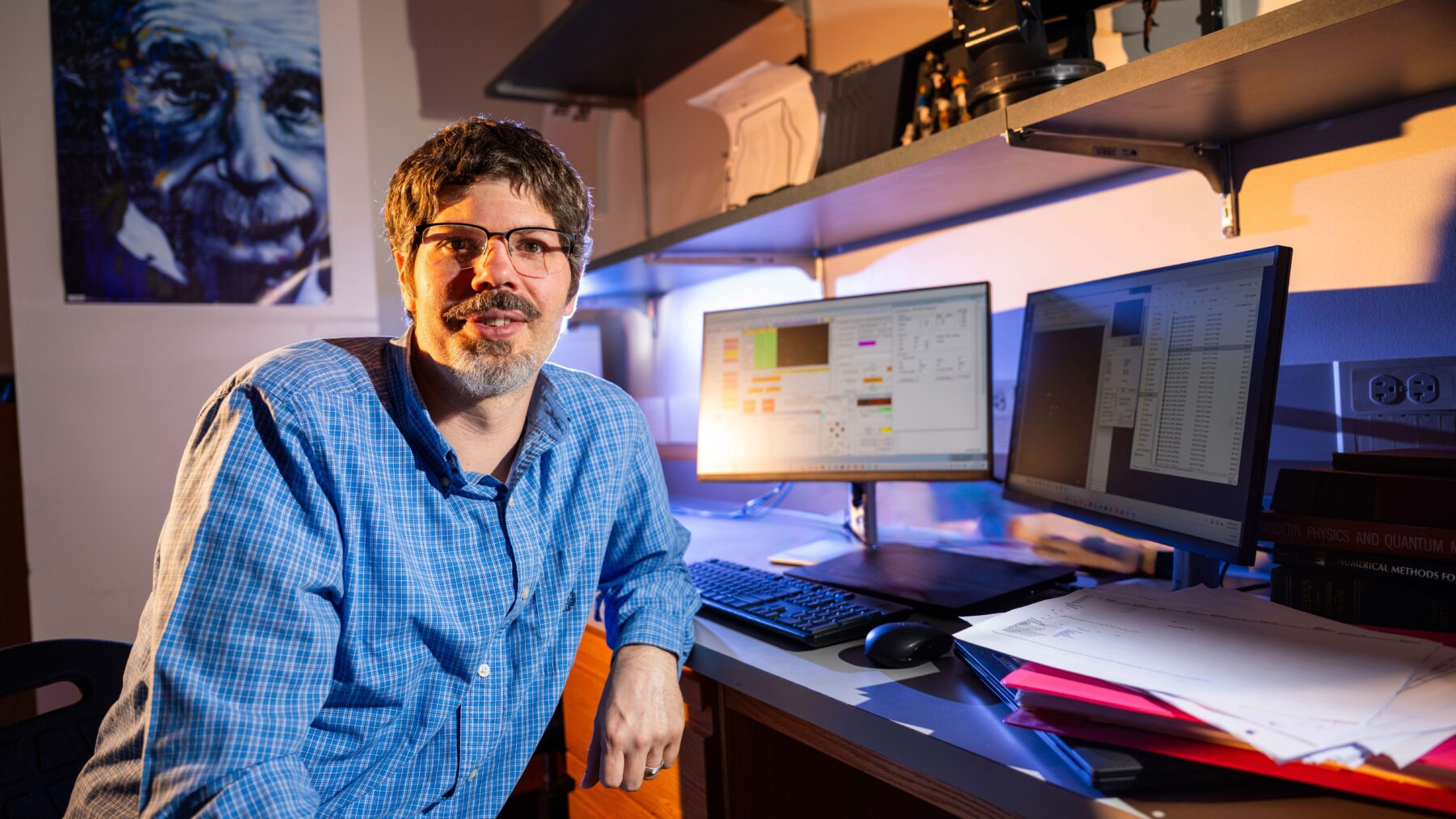 A man sitting in front of two computer monitors, smiling at the camera.