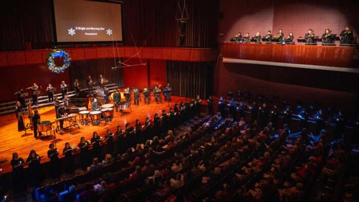 A full concert hall with a vocal and band ensemble performing.